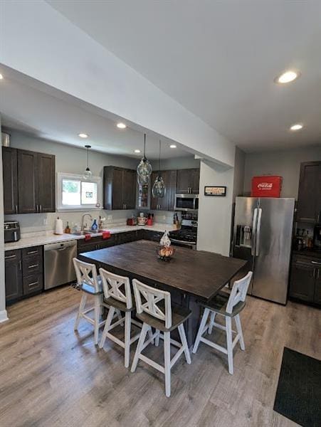 kitchen with decorative light fixtures, light hardwood / wood-style floors, dark brown cabinets, and stainless steel appliances