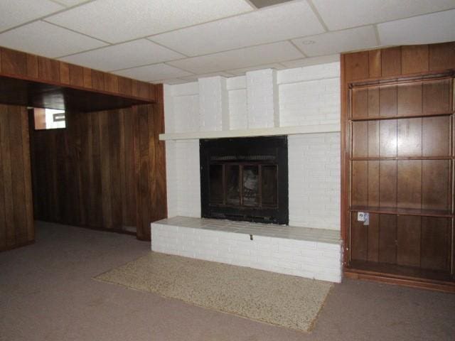 interior space with a drop ceiling, wood walls, and a brick fireplace