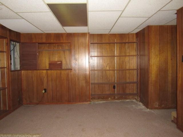 carpeted empty room with a paneled ceiling and wooden walls