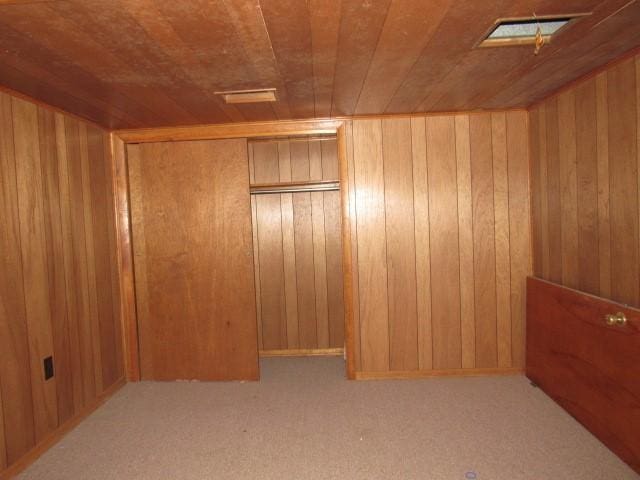 interior space with wood walls, wooden ceiling, light carpet, and a closet