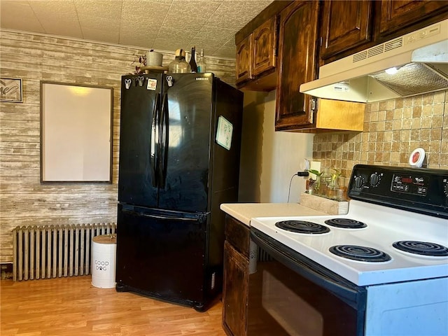 kitchen featuring white range with electric cooktop, black fridge, radiator heating unit, and wood walls