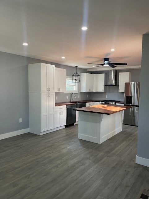 kitchen with wall chimney exhaust hood, stainless steel appliances, decorative light fixtures, white cabinetry, and butcher block counters