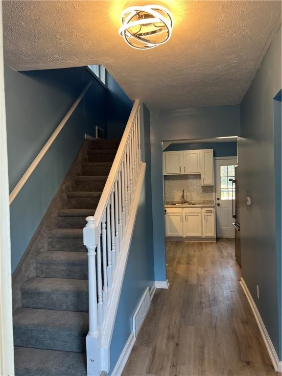 stairway featuring hardwood / wood-style floors, sink, and a textured ceiling