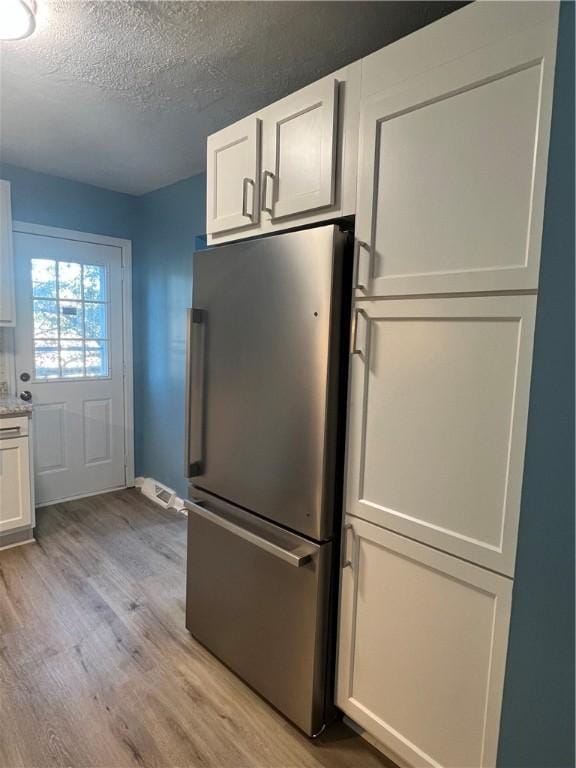 kitchen with white cabinetry, stainless steel fridge, light hardwood / wood-style flooring, and a textured ceiling