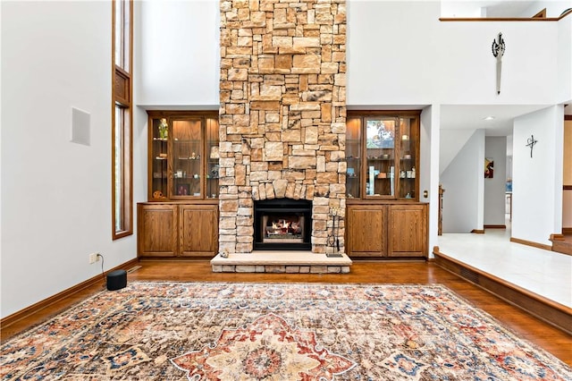 unfurnished living room featuring a stone fireplace, a high ceiling, and wood-type flooring