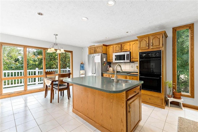 kitchen featuring backsplash, stainless steel appliances, sink, decorative light fixtures, and an island with sink