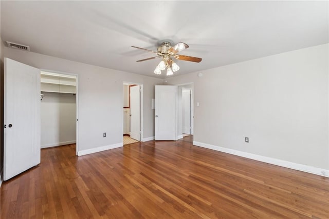 unfurnished bedroom featuring ceiling fan, a walk in closet, dark wood-type flooring, and a closet