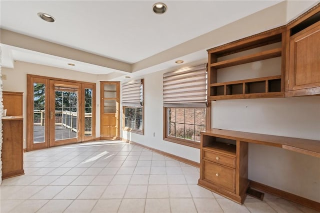 unfurnished office featuring plenty of natural light, built in desk, and light tile patterned floors