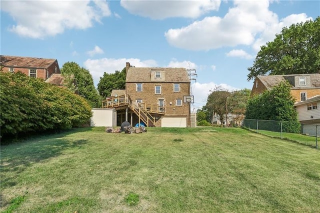 rear view of house featuring a deck, a garage, and a lawn