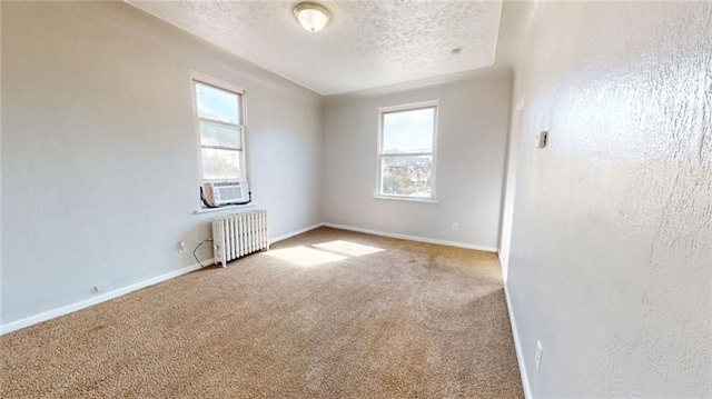 carpeted empty room with radiator, cooling unit, a healthy amount of sunlight, and a textured ceiling