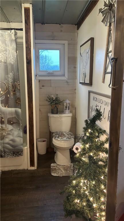 bathroom featuring hardwood / wood-style flooring, wood walls, toilet, and shower / bathtub combination with curtain