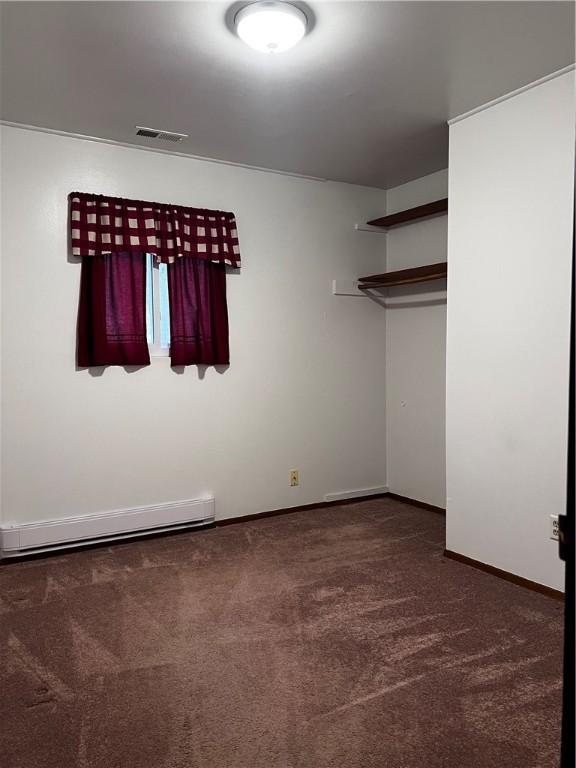 unfurnished bedroom featuring dark carpet and baseboard heating