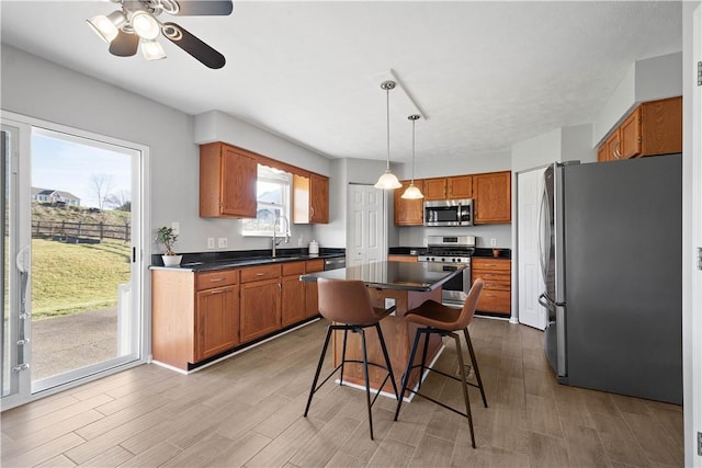 kitchen featuring appliances with stainless steel finishes, decorative light fixtures, a kitchen bar, a kitchen island, and light wood-type flooring