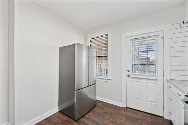 kitchen with stainless steel fridge, white cabinetry, dark wood-type flooring, and light stone counters