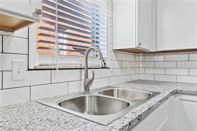 details with tasteful backsplash, white cabinetry, sink, and light stone counters