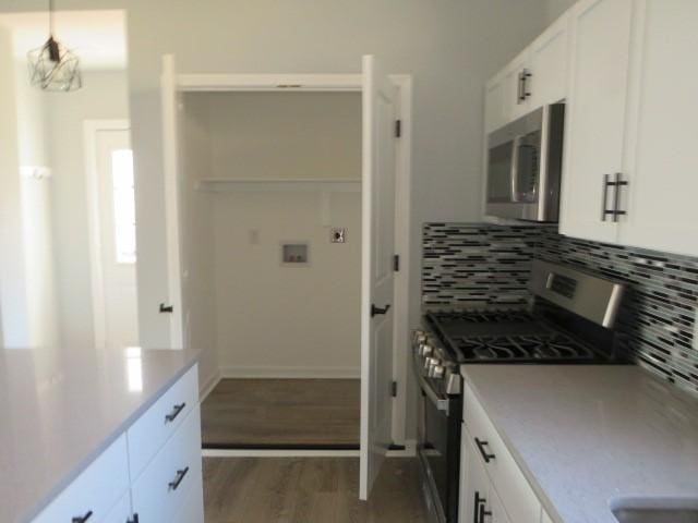 kitchen with tasteful backsplash, white cabinets, appliances with stainless steel finishes, and wood finished floors