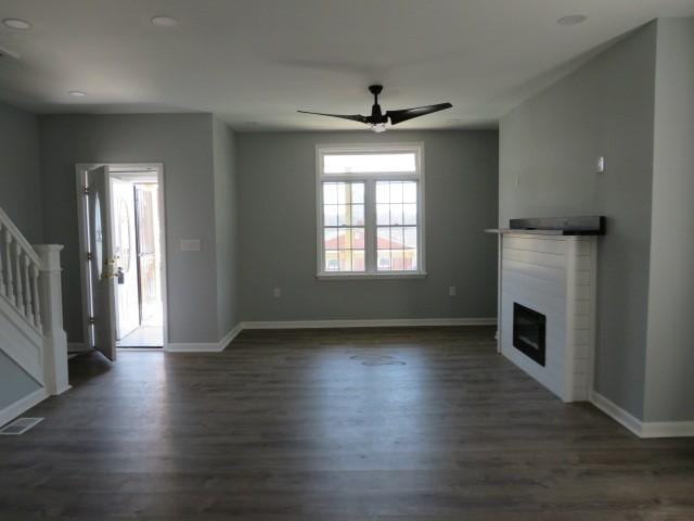 unfurnished living room with dark wood-style floors, baseboards, visible vents, stairs, and a glass covered fireplace