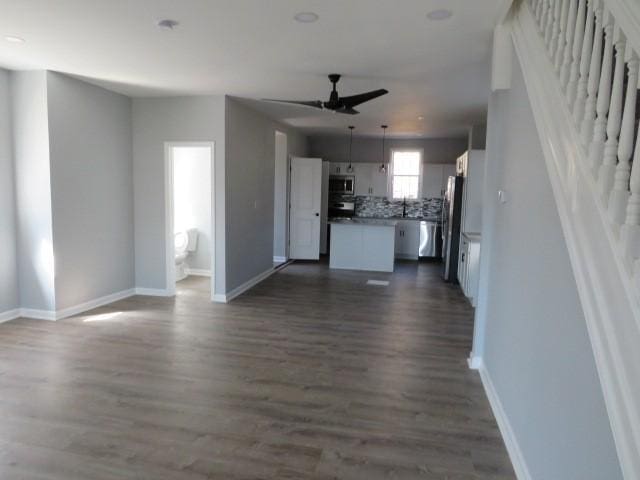 unfurnished living room featuring baseboards, dark wood-style floors, and a ceiling fan