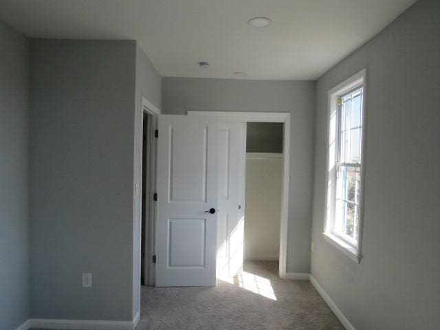 unfurnished bedroom with a closet, multiple windows, carpet floors, and baseboards