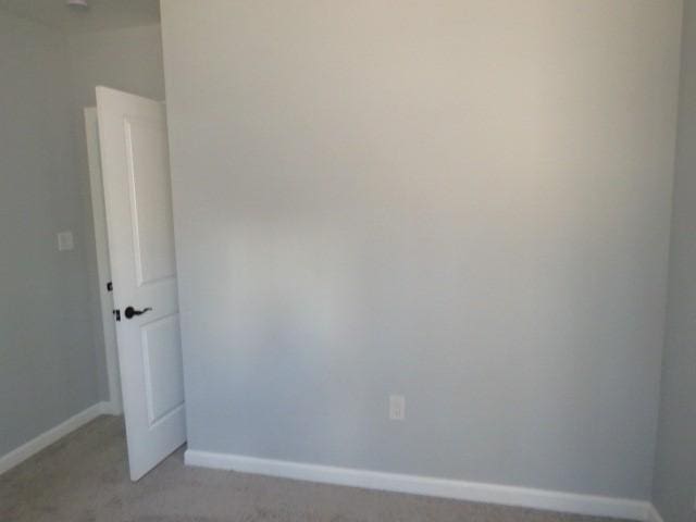 spare room featuring light colored carpet and baseboards