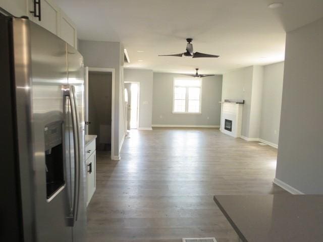 kitchen featuring baseboards, ceiling fan, wood finished floors, stainless steel fridge, and white cabinetry