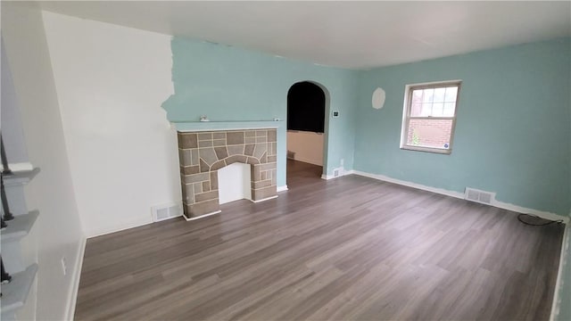 unfurnished living room featuring a stone fireplace and dark hardwood / wood-style floors