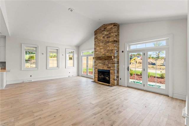 unfurnished living room featuring lofted ceiling, a healthy amount of sunlight, a stone fireplace, and light wood-type flooring