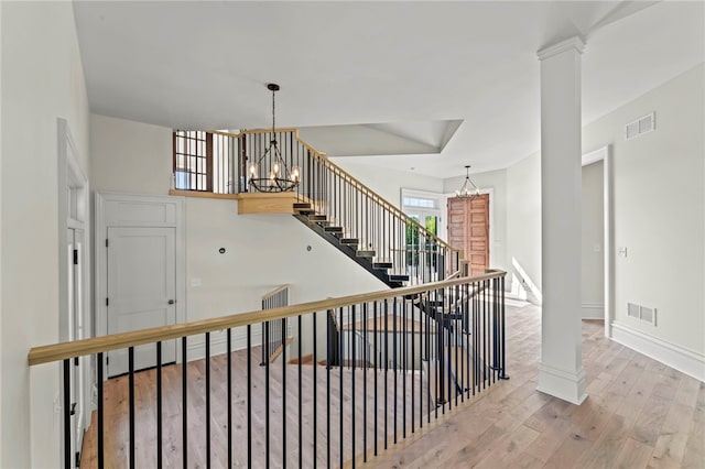 staircase with a chandelier, wood-type flooring, and decorative columns