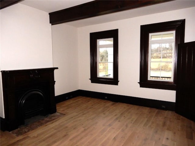 unfurnished living room featuring beamed ceiling, a healthy amount of sunlight, and hardwood / wood-style flooring