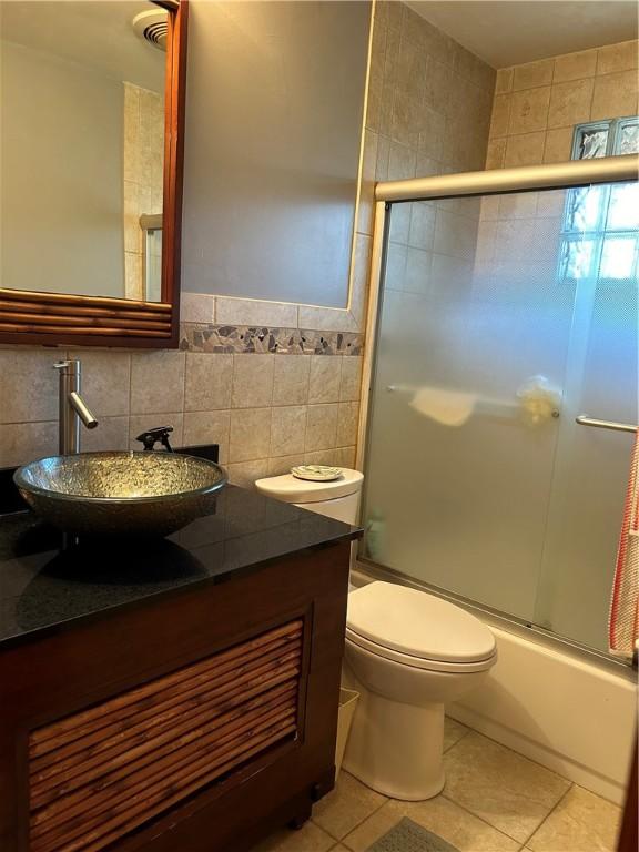 full bathroom featuring tile patterned floors, bath / shower combo with glass door, tile walls, and toilet