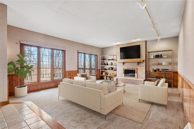 carpeted living room featuring a fireplace, track lighting, plenty of natural light, and wooden walls