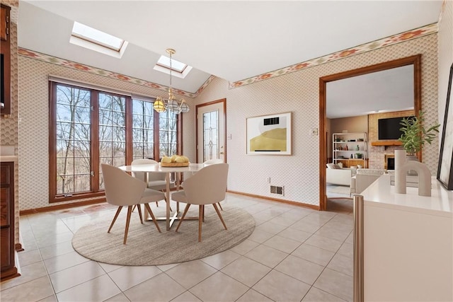 dining room with an inviting chandelier, light tile patterned floors, vaulted ceiling, and a brick fireplace