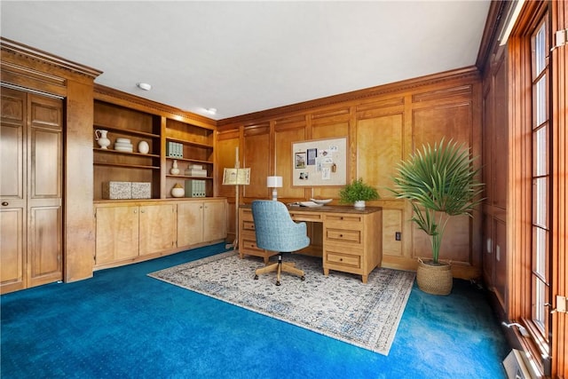 office space with built in shelves, wood walls, dark carpet, and ornamental molding