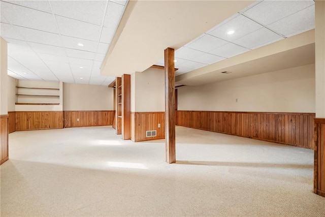 basement with a paneled ceiling, wood walls, and light carpet