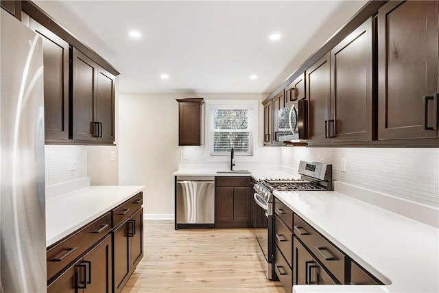 kitchen with decorative backsplash, appliances with stainless steel finishes, dark brown cabinets, sink, and light hardwood / wood-style floors