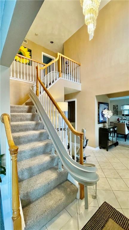 stairway with a high ceiling, an inviting chandelier, and tile patterned floors