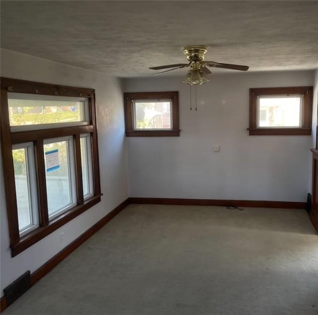 carpeted empty room with a textured ceiling, plenty of natural light, and ceiling fan