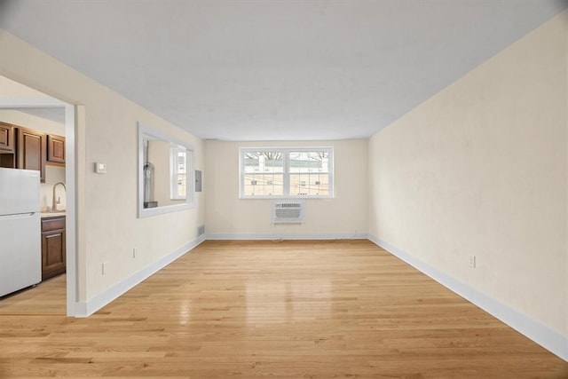 unfurnished room featuring sink, a wall unit AC, and light hardwood / wood-style flooring