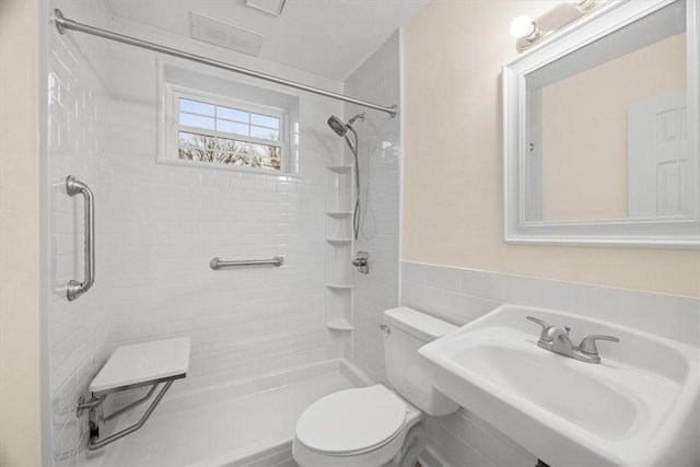 bathroom featuring a tile shower, sink, tile walls, and toilet