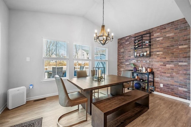 dining room with lofted ceiling, wood-type flooring, brick wall, and a chandelier