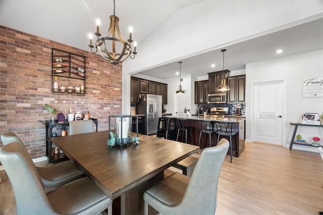 dining room featuring brick wall, sink, light hardwood / wood-style flooring, a notable chandelier, and lofted ceiling