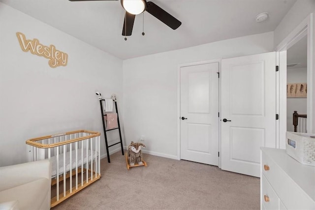 bedroom featuring light carpet, ceiling fan, and a crib