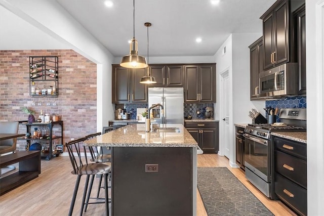 kitchen featuring light hardwood / wood-style floors, dark brown cabinetry, a kitchen island with sink, and appliances with stainless steel finishes