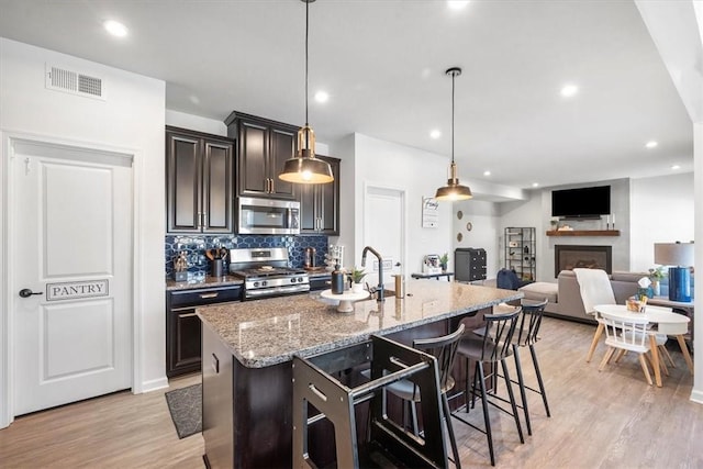 kitchen featuring a center island with sink, pendant lighting, light wood-type flooring, and appliances with stainless steel finishes