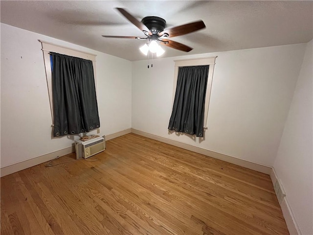 empty room with a wall mounted air conditioner, ceiling fan, and light wood-type flooring