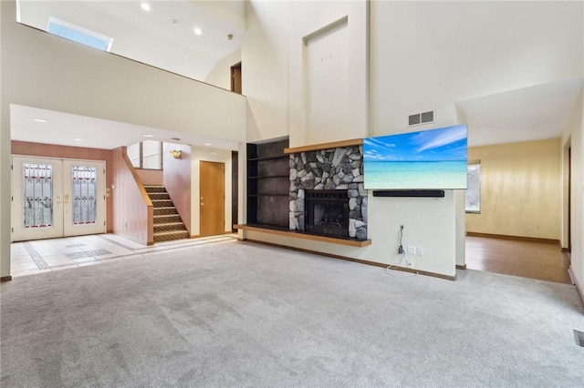 unfurnished living room with light carpet, french doors, a towering ceiling, and a stone fireplace