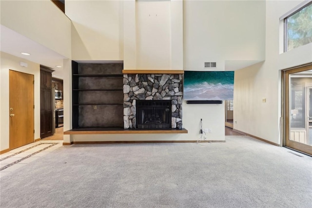 unfurnished living room featuring a stone fireplace, a wealth of natural light, a towering ceiling, and light colored carpet