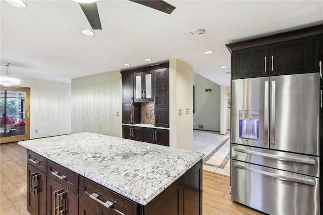 kitchen with dark brown cabinets, stainless steel fridge, a kitchen island, and light stone countertops