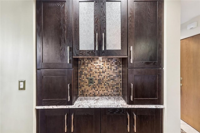 kitchen featuring light stone countertops, decorative backsplash, and dark brown cabinets