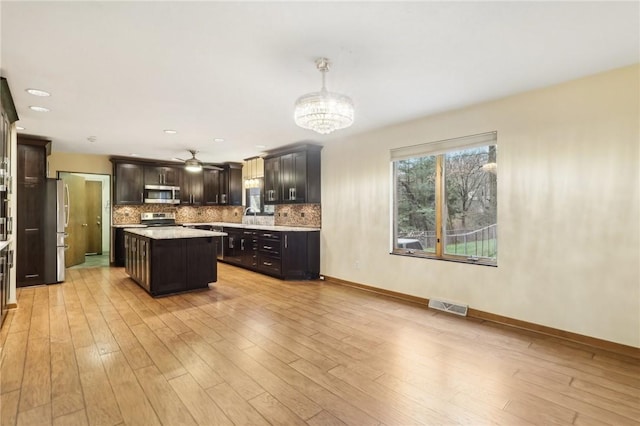 kitchen with pendant lighting, light hardwood / wood-style flooring, appliances with stainless steel finishes, dark brown cabinets, and a kitchen island